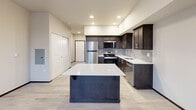 Located at 1450 Odegard Rd SW in Tumwater, Washington, this single-floor unit offers a thoughtfully designed layout that maximizes functionality within a compact footprint. Light-toned luxury vinyl plank flooring runs throughout, creating a cohesive and easy-to-maintain aesthetic accented by dark espresso-stained trim and door frames.

The open-concept kitchen and living area serves as the heart of the space. The kitchen features dark walnut-toned cabinetry, white quartz countertops, a gray subway tile backsplash, and a full suite of stainless steel appliances including a refrigerator, range, over-the-range microwave, and dishwasher. A freestanding center island with a white countertop provides additional prep space and casual seating. Recessed lighting and a window overlooking the exterior fill the area with natural light.

The den, accessed via a stylish sliding barn door, offers a flexible space suitable for a home office or additional sleeping area. The combined bathroom and laundry room is well-appointed with dark cabinetry, white quartz countertops, a wide vanity mirror with lighted surround, and efficient use of the available space. Two closets provide practical storage, while a central hallway connects the various areas of the unit seamlessly. The overall ambiance is clean, modern, and move-in ready.