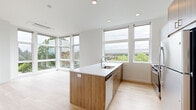This single-floor space is designed with a clean, contemporary aesthetic characterized by crisp white walls, light hardwood flooring, and an abundance of natural light. The open-plan living and kitchen area serves as the centerpiece, anchored by a substantial island featuring warm wood cabinetry and a white countertop with an integrated sink. Floor-to-ceiling windows and expansive glazed panels wrap around this area, framing elevated views of surrounding treetops and the urban skyline beyond, creating a bright and airy atmosphere throughout the day.

The hallway connects the living areas to the private rooms, which include multiple well-proportioned bedrooms. Each bedroom benefits from large windows that invite natural light and offer outdoor views, while maintaining a neutral, versatile palette. Light hardwood flooring carries consistently through every room, reinforcing a cohesive design language.

The bathrooms are finished in a clean, minimalist style, with one featuring a full soaking tub and shower combination set against white tile surround. The overall layout, as visible in the floorplan model, is efficiently organized, balancing open communal spaces with defined private zones. The space presents a fresh, move-in ready condition throughout.