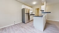 Located at 825 Trillium Park in Sarnia, Ontario, this one-bedroom, one-bathroom unit offers a well-organized and functional layout finished throughout with light-toned vinyl plank flooring and neutral warm-beige walls that create a clean, cohesive aesthetic.

The living room is a bright and open area anchored by a full-width sliding glass patio door that provides direct access to an outdoor balcony and invites natural light deep into the space. A secondary window alongside the door further enhances the airy feel and frames views of mature trees in the surrounding landscape. Baseboard heating runs along the exterior walls, ensuring year-round comfort.

The galley-style kitchen is efficiently designed with white shaker cabinetry on both sides, dark granite-style countertops, a stainless steel sink, and a classic white subway tile backsplash. A stainless steel range with overhead ventilation hood completes the culinary setup. A breakfast bar peninsula separates the kitchen from the main living area, adding a casual dining option.

The bedroom is a well-proportioned room featuring a large double bi-fold closet that provides ample storage. The four-piece bathroom is finished with large-format tile on both the floors and walls, and includes a white vanity with a single sink, a toilet, and a soaker tub with an overhead shower.