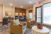 Located at 151 Integra Vistas Dr in Chattanooga, Tennessee, this single-floor community amenity space seamlessly blends a lounge area with a fully equipped business center. The open layout is anchored by a striking wood-paneled accent wall that adds warmth and texture to the contemporary interior design.

The lounge portion of the space features plush patterned armchairs, sleek marble-topped bistro tables, and rich burgundy chairs arranged to encourage both relaxed socializing and casual meetings. A wall-mounted flat-screen TV is positioned against a warm earth-toned accent wall, creating an inviting media area ideal for unwinding. Natural light filters in through large windows fitted with blinds, brightening the space throughout the day.

The business center area is defined by a built-in desk workstation along the wood accent wall, equipped with computers and a printer, and illuminated by stylish pendant lights. Framed landscape artwork adorns the walls, adding a polished, curated aesthetic throughout.

Recessed ceiling lighting provides consistent illumination across the entire space, while a combination of textured carpet flooring and structural columns reinforce the space's modern, purposeful design. The overall ambiance is professional yet comfortable, making it a versatile environment suited for both productivity and leisure.