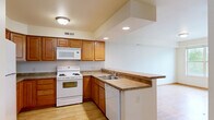 Located at 215 W Cascade Ave in River Falls, Wisconsin, this single-floor residence offers four bedrooms and three bathrooms in a well-organized layout. Light wood-style flooring runs throughout the home, creating a warm and cohesive aesthetic. The kitchen and living room share an open-concept space anchored by a peninsula counter with ample workspace. The kitchen features warm-toned wood cabinetry, recessed lighting, a vaulted ceiling accent, and white appliances including a range, built-in microwave, dishwasher, and refrigerator. A central hallway connects the four bedrooms, each finished with wood-style floors and natural light from large windows. Several bedrooms include ceiling fans, and views vary from lush greenery to the surrounding neighborhood. The spacious primary bedroom includes a generous walk-in closet equipped with wire shelving for organized storage. Three full bathrooms are finished with tile flooring, white tub-shower combinations, and wood-cabinet vanities with light countertops. A dedicated laundry room houses a full-size washer and dryer alongside the water heater and furnace, all on tile flooring. The home's clean, neutral palette and functional layout make it a practical and comfortable residence.