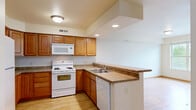 Located at 215 W Cascade Ave in River Falls, Wisconsin, this single-floor residence offers four bedrooms and three bathrooms in a well-organized layout. Light wood-style flooring runs throughout the home, creating a warm and cohesive aesthetic. The kitchen and living room share an open-concept space anchored by a peninsula counter with ample workspace. The kitchen features warm-toned wood cabinetry, recessed lighting, a vaulted ceiling accent, and white appliances including a range, built-in microwave, dishwasher, and refrigerator. A central hallway connects the four bedrooms, each finished with wood-style floors and natural light from large windows. Several bedrooms include ceiling fans, and views vary from lush greenery to the surrounding neighborhood. The spacious primary bedroom includes a generous walk-in closet equipped with wire shelving for organized storage. Three full bathrooms are finished with tile flooring, white tub-shower combinations, and wood-cabinet vanities with light countertops. A dedicated laundry room houses a full-size washer and dryer alongside the water heater and furnace, all on tile flooring. The home's clean, neutral palette and functional layout make it a practical and comfortable residence.