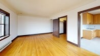 Located at 309 E Harrison St in Seattle's vibrant Capitol Hill neighborhood, this single-floor unit offers an efficient and well-organized layout comprising a living room, kitchen, hallway, closet, and bathroom. Throughout the living areas, warm honey-toned hardwood floors run continuously, complemented by rich dark wood door and window trim that lends a classic, cohesive character to the space. The living room is bright and airy, featuring multiple large double-hung windows with dark wood frames that frame sweeping views of the Seattle cityscape and surrounding streets, allowing ample natural light to fill the room. Baseboard heating units are positioned beneath the windows throughout. An adjacent area connects seamlessly to the kitchen, which is equipped with warm oak cabinetry extending to the ceiling for generous storage, a tile countertop, a stainless steel sink, and standard appliances including a gas range and refrigerator. Light tile flooring in the kitchen and hallway contrasts neatly with the hardwood in the living areas. The bathroom features classic white penny hex tile flooring and a shower-tub combination enclosed by glass doors with dark hardware, maintaining the consistent design language found throughout. A dedicated closet with hanging storage adds practical functionality to this well-appointed urban unit.