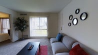 Located at 9601 Ashton Road in the Northeast Philadelphia neighborhood of PA 19114, this single-floor residential unit offers a comfortable and functional living environment. The living room serves as the heart of the space, featuring wall-to-wall carpeting that adds warmth underfoot and a large sliding glass door fitted with vertical blinds that floods the room with natural light while providing direct access to an outdoor area. The expansive window view brings in greenery from outside, creating a pleasant connection to the outdoors. The living area is laid out to comfortably accommodate seating and a central coffee table, making it well-suited for both relaxing and entertaining. Neutral-toned walls throughout lend a clean, versatile backdrop that complements a variety of décor styles. Decorative wall-mounted circular mirrors add a modern touch to the interior. A ceiling vent system ensures climate control throughout the space. The overall ambiance is bright, understated, and welcoming, with an emphasis on natural light and practical use of space — making it a solid option for those seeking a straightforward and comfortable residence in Philadelphia.