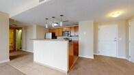 Located at 367 E Broad St in the heart of Columbus, Ohio, this single-floor unit offers a practical and well-appointed layout ideal for urban living. The open-concept kitchen and living area serves as the centerpiece of the space, featuring warm honey-toned wood cabinetry, stainless steel appliances including a refrigerator and built-in microwave, and a peninsula with a countertop overhang that provides both workspace and a casual dining option. Stylish pendant lights hang above the peninsula, adding a modern touch. The kitchen transitions seamlessly into the carpeted living area, which is lined with multiple tall windows that flood the space with natural light and offer views of the surrounding downtown Columbus cityscape. The bedroom continues the neutral color palette with soft carpet underfoot and large windows that further enhance the sense of openness. Two full bathrooms are finished consistently, each featuring warm-toned tile flooring, a vanity with white countertops and wood cabinetry, a mirror, and a full shower-tub combination. The overall aesthetic is clean and cohesive, with neutral walls and warm wood accents creating an inviting, move-in-ready environment in a prime downtown location.