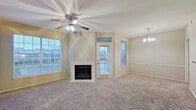 This single-story residence offers a well-organized layout across a comfortable footprint, accommodating two bedrooms, two bathrooms, a combined kitchen and living room, a dedicated laundry room, two closets, and a hallway. The living room serves as the centerpiece of the home, featuring a tile-surround wood-burning fireplace flanked by multiple windows that invite abundant natural light. A ceiling fan with integrated lighting and a decorative chandelier enhance the space, while a private exterior door provides convenient outdoor access. Plush carpeting extends throughout the living areas and bedrooms, while wood-look flooring runs through the kitchen and bathrooms.

The kitchen is efficiently designed with light wood cabinetry offering ample storage, dark laminate countertops, a double sink, a dishwasher, and a white electric range with an overhead microwave. Each bedroom is carpeted and equipped with a ceiling fan, with the primary bedroom featuring an adjoining closet. The bathrooms include vanities with laminate countertops and a tiled tub-shower combination. A dedicated laundry room houses a full-size washer and dryer, completing the practical and functional layout of this residence.