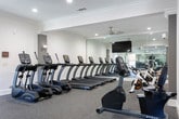 Located at 526 Dill Lane in Murfreesboro, Tennessee, this single-floor fitness center offers a comprehensive workout facility designed to accommodate a wide range of exercise needs. The space is thoughtfully organized into distinct zones, each tailored to a specific type of training.

The cardio area features a row of True-brand treadmills and elliptical machines, all positioned in front of large wall-mounted mirrors and a flat-screen television, creating an engaging environment for sustained cardio sessions. Ceiling fans and recessed lighting throughout the space ensure comfort and visibility.

The strength training zone is equipped with a True functional training cable machine, an adjustable weight bench, and a full rack of dumbbells, allowing for a variety of resistance exercises. A mirrored wall spans this area as well, supporting proper form monitoring during workouts.

A separate open exercise room provides a flexible, open-floor area ideal for stretching, yoga, or bodyweight training. This room features a ceiling fan, crown molding, speckled rubber flooring, and glass doors that allow natural light to flow in from the outdoors, connecting the interior to the surrounding environment.

Throughout the facility, durable speckled rubber flooring provides a safe, cushioned surface, while white walls with crown molding lend a clean, polished aesthetic. The inclusion of multiple windows ensures natural light permeates the space, contributing to an energizing and welcoming atmosphere.