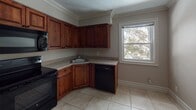 This single-floor residence offers a thoughtfully designed layout that balances functional living spaces with classic architectural details. Crown molding runs consistently throughout the home, adding a refined finishing touch to each room.

The bedrooms are generously sized, featuring neutral-toned walls, soft wall-to-wall carpeting, and bright white baseboards. Several rooms include built-in closets — one bedroom notably offers dual closets with six-panel sliding doors, while another features a single closet with a hanging rod, providing practical storage solutions. A ceiling fan with a light fixture is present in one of the bedrooms, and windows throughout allow for natural light and outdoor views of surrounding trees.

The kitchen is a functional and visually striking space, outfitted with rich, warm-toned wood cabinetry extending to the ceiling and light granite-style countertops. Black appliances — including a refrigerator, electric range, over-the-range microwave, and dishwasher — provide a cohesive, classic look. Tile flooring and a window overlooking greenery complete the kitchen's practical appeal.

The bathroom features floor-to-ceiling tile work, an oval decorative mirror, a wood vanity, and a soaking tub, lending a classic and functional character to the space.