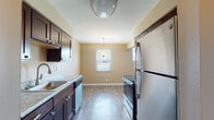 Located at 6527 Taylor Mill Rd in Independence, Kentucky, this single-floor home offers a practical and comfortable layout designed for everyday living. The galley-style kitchen is well-appointed with dark espresso cabinetry, light granite countertops, stainless steel appliances including a refrigerator, range, and dishwasher, and wood-look vinyl plank flooring. A pendant light fixture illuminates the adjacent dining area, which benefits from a window that brings in natural light. The living room is generously sized, featuring plush carpeting, a textured ceiling, and large windows that frame outdoor views and fill the space with daylight. A clean, wood-floored entry hallway provides a welcoming transition into the home. The bedrooms are comfortably proportioned with soft carpeting, neutral warm-toned walls, and windows offering natural light and outdoor views. The full bathroom is neatly finished with a white vanity, a mirrored medicine cabinet, and a tub-shower combination. Throughout the home, consistent warm beige tones, white trim, and durable flooring materials create a cohesive and move-in-ready atmosphere suited for a variety of lifestyles.