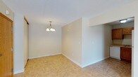 This single-floor space presents a straightforward and functional layout designed with simplicity in mind. The interior is finished in soft, neutral tones throughout, creating a calm and versatile atmosphere that can easily accommodate a variety of uses and furnishing styles.

The main living and dining area is defined by light-toned tile flooring that runs throughout, offering durability and easy maintenance. A classic multi-arm chandelier serves as a focal point overhead, providing ambient lighting to the dining or gathering area. The ceiling features a textured finish, adding subtle character to the space.

Partial walls and open passageways divide the interior into distinct zones while maintaining an open and connected feel. Clean white baseboards line the perimeter, adding a crisp contrast to the warm wall tones. The layout flows naturally between areas, maximizing usable space within the single-floor footprint.

The overall ambiance is bright and neutral, providing a blank canvas well-suited for personalization. Whether used as a residential or functional space, the clean lines, understated finishes, and practical design make this an adaptable and move-in-ready environment.