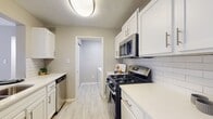 This single-floor apartment showcases a blend of modern amenities and comfortable living spaces. The kitchen boasts a sleek design with white cabinetry, subway tile backsplash, and stainless steel appliances including a gas range and over-the-range microwave. The living area features plush carpeting and a cozy fireplace, while the bedroom offers ample space and natural light from a large window. The bathroom has been updated with a contemporary vanity and a shower/tub combination. Light wood-look flooring in the kitchen and bathroom adds warmth to the overall neutral color palette, creating a fresh and inviting atmosphere throughout the apartment.
