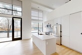 Located at 1521 Hooker St in Denver's West Colfax neighborhood, this contemporary two-floor residence offers a thoughtfully designed open layout spread across two well-proportioned levels. The main floor makes a striking first impression with soaring double-height ceilings, light hardwood flooring, and expansive floor-to-ceiling windows that flood the space with natural light and offer views of the surrounding Denver streetscape. The open-concept kitchen is a standout feature, centered around a large white waterfall island with an undermount sink. Crisp white cabinetry extends to the ceiling, complemented by stainless steel appliances including a French door refrigerator, built-in microwave, and range. An in-unit washer and dryer stack is conveniently tucked within the kitchen area. The main level also includes an open living area with a ceiling fan and direct access to a private balcony. A staircase leads to the upper level, where the generously sized primary bedroom features plush carpet, a ceiling fan, large windows with neighborhood views, and a wall of built-in cabinetry with integrated drawers for ample storage. The full bathroom presents a clean, minimalist aesthetic with a dual-sink floating vanity, dark hardware accents, and a frameless mirror. A separate room on the upper level with hardwood floors and an open closet system offers flexible use as a secondary sleeping or living space.