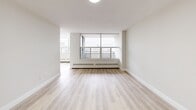 Located in Thorncliffe Park, Toronto, this well-appointed one-bedroom, one-bathroom unit offers a bright and functional layout with light hardwood-style flooring and a clean, neutral palette throughout. The open living area is generously sized across two connected spaces, bathed in natural light from large floor-to-ceiling windows that frame sweeping views of the Toronto skyline and surrounding neighbourhood. A sliding door leads to a private balcony, extending the living space outdoors. The galley-style kitchen is efficiently designed with sleek white cabinetry, stone-look countertops, a subway tile backsplash, and a full suite of stainless steel appliances including a bottom-freezer refrigerator, electric range, built-in microwave, and dishwasher. The spacious primary bedroom features a large window with city views, a dedicated closet with built-in shelving, and access to additional storage via a walk-in closet area. The bathroom is finished with a full soaker tub and shower, white tile surround, and clean chrome fixtures. Two hallways connect the rooms seamlessly, and baseboard heating is present throughout. The overall ambiance is modern, bright, and move-in ready.
