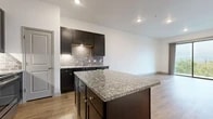 This single-floor residence is thoughtfully designed with a cohesive aesthetic that balances modern finishes with functional layout. The kitchen serves as the visual centerpiece, featuring rich dark espresso cabinetry paired with a grey subway tile backsplash and granite countertops that extend across both the perimeter surfaces and a generously sized central island. Stainless steel appliances, including a refrigerator, range, and over-the-range microwave, complement the kitchen's contemporary styling. Recessed lighting illuminates the space efficiently throughout.

Wood-look flooring runs through the main living and kitchen areas, providing warmth and visual continuity, while select rooms feature plush carpeting for added comfort. The open-concept layout connects the kitchen to a spacious living area, offering a flexible and airy feel. A hallway leads to the bedroom wing, where one room includes access to a generous walk-in closet outfitted with dual hanging rods along two walls, offering substantial storage capacity.

The bathroom is finished consistently with the kitchen, showcasing dark vanity cabinetry, granite countertops, a large mirror, and a full tub-shower combination. Light-toned wood-look flooring ties the bathroom's design to the rest of the unit, creating a unified, polished interior throughout.