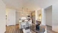 This single-floor residence is defined by a clean, contemporary design that balances functionality with modern aesthetics throughout. The open-concept kitchen serves as a central feature, showcasing light wood cabinetry that extends floor to ceiling, a marble-style tile backsplash, and a full suite of stainless steel appliances including a gas range, built-in microwave, dishwasher, and French door refrigerator. A spacious island with a white quartz countertop provides seating for multiple guests and flows naturally into the dining and living areas. A dedicated nook adjacent to the kitchen offers a convenient built-in workspace. The living room is bright and welcoming, with natural light streaming through large windows and a glass door leading to a balcony. Wood-look flooring runs consistently throughout the main living spaces, reinforcing the cohesive design. The primary bedroom is generously sized with a large window and direct access to an en-suite bathroom featuring a double-sink vanity with quartz countertops and a glass-enclosed walk-in shower. A second bedroom offers comfortable proportions and ample natural light, served by a well-appointed full bathroom with a tub-shower combination and matching light wood vanity.