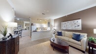 This single-floor residence offers a thoughtfully designed open-concept layout that seamlessly connects the living, dining, and kitchen areas. The spacious living room features plush carpeting, crown molding, and a warm neutral color palette accented by a taupe feature wall, creating an inviting and comfortable atmosphere. A breakfast bar peninsula separates the living area from the galley-style kitchen, which is equipped with white cabinetry, granite-look countertops, a stainless steel sink, and white appliances including an electric range and built-in microwave. Track lighting overhead provides practical illumination throughout the kitchen. The dining area is conveniently situated adjacent to the kitchen and living space, with access to an in-unit laundry closet that adds everyday convenience. The primary bedroom features vaulted ceilings, a ceiling fan, plush carpeting, and windows that allow natural light to fill the room. A second bedroom offers a bold teal accent wall and soft carpeted flooring, lending a distinct and cozy character. The full bathroom is finished with wood-look flooring, white cabinetry, and a tub-shower combination. Crown molding details are carried throughout the common areas, contributing to a cohesive and polished finish across the entire residence.