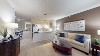 This single-floor residence offers a thoughtfully designed open-concept layout that seamlessly connects the living, dining, and kitchen areas. The spacious living room features plush carpeting, crown molding, and a warm neutral color palette accented by a taupe feature wall, creating an inviting and comfortable atmosphere. A breakfast bar peninsula separates the living area from the galley-style kitchen, which is equipped with white cabinetry, granite-look countertops, a stainless steel sink, and white appliances including an electric range and built-in microwave. Track lighting overhead provides practical illumination throughout the kitchen. The dining area is conveniently situated adjacent to the kitchen and living space, with access to an in-unit laundry closet that adds everyday convenience. The primary bedroom features vaulted ceilings, a ceiling fan, plush carpeting, and windows that allow natural light to fill the room. A second bedroom offers a bold teal accent wall and soft carpeted flooring, lending a distinct and cozy character. The full bathroom is finished with wood-look flooring, white cabinetry, and a tub-shower combination. Crown molding details are carried throughout the common areas, contributing to a cohesive and polished finish across the entire residence.