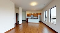 This thoughtfully designed single-floor residence offers a seamless open-concept layout that connects the living area and kitchen, creating a generous and airy atmosphere. Warm hardwood flooring flows throughout the main living spaces, complemented by clean white walls and rich wood trim that lend a contemporary yet inviting character.

The kitchen is a standout feature, showcasing rich wood cabinetry, dark granite countertops, and a full suite of stainless steel appliances including a refrigerator, range, microwave, and dishwasher. A central island with an integrated sink provides additional workspace and doubles as a casual dining or gathering area. Track and pendant lighting illuminate the space with a modern touch.

The bedrooms are carpeted for comfort and benefit from generous natural light. The primary bedroom includes access to a private balcony through large sliding glass doors, offering views of the surrounding urban landscape. A spacious walk-in closet with wire shelving provides ample storage. A secondary bedroom features its own closet and easy access to the hallway.

Two bathrooms serve the residence: a full bath with a soaking tub and tiled flooring, and a primary bath featuring a glass-enclosed walk-in shower, wide vanity, and large-format tile floors. The overall ambiance is clean, modern, and functional.