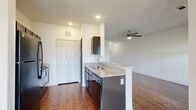 Located at 8618 Vertex Blvd in Austin, TX, this one-bedroom, one-bathroom residence offers a well-designed single-floor layout with a cohesive, modern aesthetic throughout. Rich, dark hardwood-style flooring flows seamlessly across every room, lending warmth and continuity to the space.

The open living room is bright and airy, featuring elevated ceilings, a ceiling fan with light fixture, and large windows paired with a glass-paneled door that fills the space with natural light and provides views of the surrounding greenery. A peninsula counter connects the living area to the kitchen, which is outfitted with dark cabinetry, granite-style countertops, a stainless steel sink, black appliances, and a spacious double-door closet for additional storage.

The bedroom is generously sized, continuing the hardwood-style flooring and elevated ceiling design, with a ceiling fan, large window for natural light, and a double-door closet offering ample storage.

The bathroom is well-appointed with dark wood cabinetry, a granite-top vanity, a glass-enclosed walk-in shower, and matching hardwood-style flooring. Grab bars add a practical accessibility feature.

Outside, the property features a well-maintained lawn with open, expansive views of the surrounding landscape under the wide Texas sky.