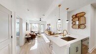 Located on Christopher Court in Arden, NC, this thoughtfully designed 2-bedroom, 2-bathroom residence offers a bright, modern living experience across a single floor. The open-concept layout seamlessly connects the kitchen, dining, and living areas, all finished with light wood-look flooring that enhances the airy, sun-filled atmosphere. The kitchen is a standout feature, boasting a quartz waterfall island with bar seating, gold-accented fixtures, a undermount sink, stainless steel appliances including a French door refrigerator and range, and light wood cabinetry accented by stylish pendant lighting. The living room flows naturally from the kitchen and opens to a private balcony, inviting natural light through large windows. Both bedrooms are carpeted and well-proportioned, each with ceiling fans and generous closet space. The primary bedroom connects to an en-suite bathroom featuring a dual-sink vanity with light wood cabinetry, gold hardware, and a glass-enclosed shower. The second bathroom offers a combination tub and shower. Additional conveniences include in-unit laundry, multiple hallways for smooth circulation, and ample closet storage throughout. The overall aesthetic is clean and contemporary, blending warm neutrals with modern gold and black accents.
