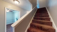 This two-story home offers 2 bedrooms and 2.5 bathrooms across a well-organized floor plan. The main level features rich, warm-toned hardwood-style flooring that flows through the living areas and kitchen. The galley-style kitchen is equipped with white cabinetry, gray countertops, a double sink, and white appliances including a range and refrigerator, with natural light streaming in through a window. Crown molding and textured ceilings add a classic touch to the main living area, which also includes a ceiling fan and a window with blinds. A half bathroom on the main floor adds convenience for guests. A carpeted staircase with a white handrail connects the two floors. Upstairs, the two bedrooms are finished with plush carpet and gray-toned walls, each featuring windows with blinds that invite natural light. The primary bedroom includes a ceiling fan and access to a closet. The two full bathrooms feature a tub-shower combination, white cabinetry with storage above, a single vanity with gray countertops, and hardwood-style flooring. The home's neutral gray palette and consistent finishes throughout create a cohesive and functional living environment.
