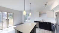 This thoughtfully designed 1-bedroom, 2-bathroom residence with a den offers a modern, open-concept layout that maximizes both function and comfort on a single floor. The kitchen is a standout feature, showcasing dark cabinetry contrasted by a light quartz countertop island, stainless steel appliances including a dishwasher, and a sleek undermount sink. Two elegant pendant lights hang above the island, adding warmth and a refined aesthetic to the space. Light hardwood-style flooring flows throughout, complementing the neutral, bright color palette. Large windows invite generous natural light into the open living and dining area, offering pleasant views of lush greenery outside. The airy, high ceilings further enhance the sense of openness throughout the home. The addition of a den provides flexible space ideal for a home office, reading nook, or guest room. With two full bathrooms, the layout is both practical and accommodating. The overall ambiance is clean, contemporary, and welcoming, making this residence a comfortable and stylish place to call home.