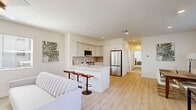 Located at 5181 Monte Vista Dr in Riverside, California, this well-appointed 2-bedroom, 2-bathroom residence offers a thoughtfully designed single-floor layout with modern finishes throughout. The open-concept living, dining, and kitchen area forms the heart of the home, where light wood-style flooring flows seamlessly underfoot. The kitchen is outfitted with crisp white cabinetry, a neutral tile backsplash, stainless steel appliances including a French door refrigerator and over-the-range microwave, and a clean white countertop with a contemporary sink and faucet. The dining area benefits from large windows dressed with white blinds, inviting ample natural light and neighborhood views. The living room continues the bright, airy aesthetic with additional windows and light-toned walls. The spacious primary bedroom features plush carpeting, a ceiling fan, and its own en-suite bathroom complete with a white vanity and easy access. The second bedroom is equally comfortable with carpeted floors, a ceiling fan, and a window overlooking the surroundings. Both bathrooms are finished in a clean, modern style — one showcasing a striking marble-tiled walk-in shower with sliding glass doors, light wood flooring, and built-in shelving niches.