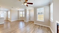 Located in D'Iberville, Mississippi, this well-appointed 3-bedroom, 3-bathroom single-story home offers a thoughtfully designed layout with a blend of comfort and practicality. The open living room greets you with gleaming hardwood-style flooring, crown molding, abundant natural light from large windows, and a ceiling fan overhead — creating a bright, welcoming atmosphere. The kitchen is equipped with stainless steel appliances, white cabinetry, and a direct-access balcony door flanked by sun-filled windows, perfect for enjoying outdoor views. The balcony itself features classic brick exterior accents, metal railings, and a pleasant view of the landscaped yard. Each of the three bedrooms is carpeted for comfort and equipped with a ceiling fan, with the generously sized primary bedroom offering walk-in closet space complete with wire shelving. The three bathrooms are finished with white vanities, brushed nickel fixtures, and well-lit mirrors, while at least one bathroom includes a full soaking tub with tiled surround. A private attached garage with a concrete floor and interior access door provides convenient parking and additional storage. Neutral warm-toned walls throughout the home create a cohesive, move-in ready aesthetic.