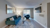 This thoughtfully designed 1-bedroom, 1-bathroom single-floor residence offers an efficient yet comfortable layout across a compact footprint. The living room serves as the heart of the home, featuring wood-style flooring, neutral gray walls, a large sliding glass door that floods the space with natural light, and direct access to an outdoor area. A wall-mounted mirror and a textured ceiling add visual depth to the room.

Adjacent to the living area, the dining space accommodates an intimate round glass-top table for two, accented by warm neutral tones and contemporary abstract wall art. The galley-style kitchen is equipped with warm wood cabinetry, black appliances including a full-size refrigerator and electric range, light countertops, and a built-in dishwasher — offering functional efficiency in a compact form.

The bedroom is carpeted and serene, receiving natural light through a window with blinds. It connects directly to a dedicated closet, providing practical storage. The full bathroom features a clean, bright aesthetic with a tiled shower-tub combination, light wood-style flooring, and a vanity area. Two hallways connect the spaces seamlessly, contributing to a logical and easy-to-navigate floor plan throughout the residence.