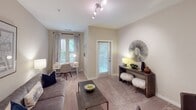 This single-floor residence is thoughtfully designed with a neutral color palette and a layout that promotes comfortable, everyday living. The kitchen serves as a functional centerpiece, featuring dark espresso cabinetry that extends to the ceiling, granite countertops, stainless steel appliances including a refrigerator, range, and microwave, and rich hardwood-style flooring. A peninsula with bar seating connects the kitchen to the adjacent dining area, where plush carpet begins and a glass-top table with modern chairs occupies the space beneath a set of decorative wall art panels. The living room is carpeted and receives natural light through multiple windows and a glass door providing direct patio access, creating an airy, welcoming atmosphere. Track lighting adds a contemporary touch overhead. The primary bedroom is generously proportioned, with soft carpet, a ceiling fan, and windows that invite natural light and outdoor views. A second bedroom offers a similarly calm and cozy retreat. The shared bathroom features tile flooring and a soaking tub-shower combination. A hallway connects the main living spaces to the bedrooms, with additional closet storage along its length.