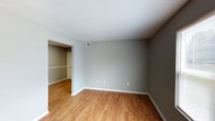 This single-story residence offers three bedrooms and two bathrooms within a thoughtfully organized layout. Throughout the home, neutral gray walls and white trim create a clean, cohesive aesthetic. The living and entry areas feature warm wood-look laminate flooring, while a large front window allows generous natural light to fill the space. The front entry door is solid and paneled, contributing to a functional, no-frills design.

The galley-style kitchen is a standout feature, lined on both sides with rich, dark espresso cabinetry that provides ample upper and lower storage. Light granite-style countertops contrast the dark wood tones, and a stainless steel sink anchors one side of the counter. White appliances, including a range and refrigerator, are included. A recessed skylight-style ceiling fixture illuminates the kitchen efficiently.

Each of the three bedrooms is carpeted in neutral beige tones and features a closet with built-in shelving rods for organization. The bedrooms maintain a consistent design language with gray walls, textured ceilings, and ceiling-mounted light fixtures. Windows in several bedrooms provide natural light and ventilation. The overall ambiance is clean, practical, and move-in ready.