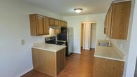 This single-floor space offers a well-designed layout centered around a functional, open-concept kitchen and dining area. The kitchen is outfitted with warm-toned oak cabinetry providing generous upper and lower storage, complemented by light countertops that offer ample prep space. A double-basin sink, electric range, dishwasher, and a full-size refrigerator make up the appliance suite, while a peninsula-style counter adds additional workspace and casual seating potential. The kitchen flows naturally into the adjoining dining area, which is finished with rich hardwood-style flooring that extends throughout the space, adding warmth and cohesion. A ceiling fan with a light fixture anchors the dining area, promoting air circulation and comfort. A window overlooking the exterior allows natural light to fill the space, brightening the open layout. A textured ceiling adds subtle visual depth. A bifold-door closet adjacent to the kitchen provides convenient storage. The overall ambiance is practical and comfortable, with a neutral color palette that creates a versatile backdrop suited to a variety of interior styles.