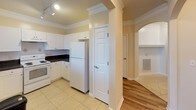 This single-floor residence showcases a thoughtfully designed layout with consistent architectural details throughout, including elegant crown molding and warm neutral tones that create a cohesive, welcoming ambiance. The living area features rich hardwood-style flooring, wainscoting panels, and track lighting, with a glass door opening to a private balcony that brings in generous natural light and outdoor views of surrounding greenery. The kitchen is well-equipped with white cabinetry, dark granite-style countertops, a tile backsplash, white appliances including a range and refrigerator, and light tile flooring. A decorative arched column separates the kitchen from the adjoining living space. The bedrooms are carpeted and each features a ceiling fan, crown molding, and large windows overlooking the neighborhood and treetops. One bedroom includes direct access to a private balcony. The primary bathroom offers an extended vanity with dual sinks, tile flooring, and a soaking tub with a shower, while the secondary bathroom features a long single-sink vanity with a large mirror and tile flooring. A spacious walk-in closet with built-in shelving provides ample storage. A dedicated laundry room accommodates a full-size washer and dryer, completing this functional and comfortable home.