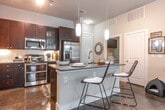 This single-story residence features a contemporary design with a cohesive neutral palette and polished concrete flooring throughout the main living areas. The open-concept kitchen is a standout, showcasing rich dark espresso cabinetry, light quartz countertops, a full suite of stainless steel appliances, and a large center island with seating. Pendant lighting and under-cabinet illumination add depth, while a dedicated laundry area with side-by-side washer and dryer and overhead cabinetry is conveniently accessible nearby.

The living room benefits from elevated ceilings, a ceiling fan, and large windows that invite natural light. The space flows seamlessly, offering a comfortable and versatile layout.

The bedrooms are carpeted and generously proportioned, with notable ceiling height adding an airy quality. One bedroom includes a walk-in closet, providing ample storage. The bathrooms are distinctly finished: one features a glass-enclosed wet area with a soaking tub and mosaic tile flooring, while the other includes a large vanity mirror with bold lighting and direct access to the walk-in closet. Together, the rooms deliver a well-balanced, modern living environment.