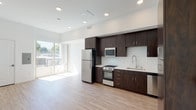 Located at 7370 S La Tijera Blvd in Los Angeles, this single-floor unit showcases a clean, contemporary design with an open-concept layout that seamlessly integrates the kitchen and living areas. Light wood-tone flooring runs throughout, complementing the bright white walls and recessed lighting to create an airy, well-lit atmosphere.

The kitchen is a standout feature, fitted with rich dark-espresso cabinetry that extends to the ceiling for ample storage. Stainless steel appliances include a full-size refrigerator, gas range, built-in microwave, and dishwasher, all set against a white tile backsplash and light countertops. A tall pantry-style cabinet near the entry provides additional storage.

The open living area benefits from generous natural light streaming through large sliding glass doors that lead to a private balcony, offering outdoor views of the surrounding Los Angeles landscape. The space feels expansive and versatile, with clean, unadorned walls ready to accommodate a variety of furniture arrangements.

A separate room provides a quiet, enclosed retreat with its own recessed lighting and wood flooring. The bathroom features tiled floors and a shower enclosure. Overall, the unit presents a modern, functional aesthetic well-suited for urban living in the Westchester neighborhood of Los Angeles.