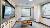 Located at 120 Matheson Ave in Charlotte, NC, this thoughtfully designed single-floor space blends modern aesthetics with vibrant, artistic character. The layout includes a meeting room, an intimate seating nook, and a bathroom, making it well-suited for collaborative or private use.

The meeting room is a standout feature, anchored by a sleek dark-topped conference table paired with stylish rattan-accented chairs. Two large black-framed windows flood the room with natural light and offer views of the surrounding streetscape. A wall-mounted display screen sits against a lively, illustrated wallpaper featuring colorful character portraits, adding a playful and creative energy to the space.

The central corridor connects the rooms with deep navy blue walls, patterned carpet tile flooring, and glass-paneled doors with dark metal frames — a clean, contemporary aesthetic that runs throughout. A cozy dining nook is tucked against a wood-paneled wall, outfitted with a green upholstered booth, a small table, and a pendant light overhead, creating a warm and intimate atmosphere.

Additional character is found in an open alcove accented with bold, graphic wallpaper, housing a single lounge chair — ideal as a quiet retreat. Recessed lighting throughout ensures a well-lit environment, while the curated artwork and décor give the space a distinctly creative and welcoming ambiance.