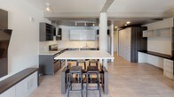 Located at 78 Ionia Ave NW in the heart of downtown Grand Rapids, Michigan, this single-floor unit showcases a sleek, modern design with a cohesive aesthetic throughout. Light wood-style tile flooring runs continuously across the space, enhancing the sense of openness and flow.

The kitchen is a standout feature, designed with a contemporary edge. Dark gray lower cabinetry is paired with high-gloss white upper cabinets, creating a striking contrast. A stone-look backsplash adds texture, while stainless steel appliances—including a refrigerator, dishwasher, and range—provide a polished, functional finish. A large white-topped kitchen island with industrial-style metal stools serves as both a workspace and casual dining area, anchoring the open-concept layout.

The living area is bright and airy, benefiting from multiple large windows that frame views of the surrounding downtown Grand Rapids cityscape. Exposed concrete ceiling beams add an industrial character, while built-in shelving and cabinetry offer practical storage solutions.

The bathroom is clean and well-appointed, featuring light tile flooring, a tub and shower combination with sliding glass doors, and a vanity topped with stone-look counters. Throughout, the unit maintains a consistent, contemporary urban aesthetic.