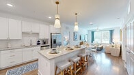 Located at 2080 Griffon Rd in Vero Beach, Florida, this single-story, two-bedroom, two-bathroom residence offers a well-designed open-concept floor plan with a cohesive coastal aesthetic. Warm hardwood-style flooring flows throughout the main living areas, anchoring the bright, neutral palette that defines the interior.

The kitchen serves as the heart of the home, featuring crisp white cabinetry, stainless steel appliances, and a granite-topped central island illuminated by a pair of gold-accented pendant lights. The island provides casual seating and transitions naturally into the adjoining dining and living areas, creating a connected, functional space well-suited for entertaining.

The living room offers natural light through multiple windows dressed with tailored drapes, and provides direct access to a screened outdoor porch. The dining area accommodates a full table and connects seamlessly to the living space.

Both bedrooms are generously proportioned with ceiling fans, ample natural light, and outdoor views. The primary suite includes an en-suite bathroom with a granite-topped vanity, walk-in glass shower, and a spacious walk-in closet. The second bathroom mirrors the same quality finishes. The overall ambiance is light, airy, and distinctly coastal.