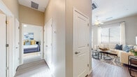 This single-floor residence presents a thoughtfully designed open-concept layout finished with light wood-style flooring and neutral-toned walls throughout. The kitchen is well-equipped with stainless steel appliances, including a range and over-the-range microwave, complemented by crisp white cabinetry, sleek hardware, and striking marble-style countertops. Natural light filters in through a window above the sink, enhancing the clean, modern aesthetic. The living area is generously sized, featuring a ceiling fan, large windows that invite abundant natural light, and direct access to the outdoors through a glass-paneled door. A dedicated dining nook sits adjacent, offering a casual space for meals. The bedrooms are comfortably proportioned, each with windows dressed in blinds and curtains. The primary suite connects to a well-designed bathroom featuring a dual-sink vanity with light countertops, white cabinetry, a glass-enclosed shower, and a walk-in closet. A central hallway connects the living spaces to the private rooms, maintaining a functional and organized flow. The overall ambiance is modern, bright, and cohesive, with consistent finishes unifying the entire space.