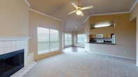 This single-floor residence is thoughtfully designed with an open, airy layout that maximizes both space and natural light. The living area serves as the heart of the home, showcasing soaring vaulted ceilings accented by crown molding and a ceiling fan with light fixture. A tile-surround fireplace anchors one wall, while large windows flood the room with natural light. A sliding glass door provides direct access to a private outdoor deck, enhancing the indoor-outdoor connection. Soft carpet flows throughout the living and bedroom areas.

The kitchen is efficiently laid out with warm wood cabinetry, dark granite-style countertops, and white appliances including a stove, microwave, and refrigerator. A raised breakfast bar opens the kitchen to the living area, creating a seamless flow. Rich hardwood-style flooring extends through the kitchen and hallways.

The bedrooms are generously proportioned, each featuring plush carpet, ceiling fans, and ample natural light from well-placed windows. One bedroom offers corner windows and another includes an en-suite walk-in closet with direct bathroom access. The bathrooms are finished with dark countertops, white cabinetry, and tub-shower combinations featuring sliding glass doors, complemented by hardwood-style flooring.