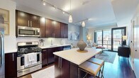 Located in Chicago's vibrant West Loop neighborhood, this 1-bedroom, 1-bathroom residence at 922 W Washington Blvd offers a thoughtfully designed open-concept layout. Rich hardwood flooring flows throughout the main living area, anchoring the contemporary aesthetic. The chef's kitchen is appointed with dark espresso cabinetry extending to the ceiling, stainless steel appliances, a gas range, and a white quartz-topped island with bar seating — all illuminated by stylish pendant lighting and a track lighting system. The kitchen opens seamlessly into the living room, where floor-to-ceiling windows and a glass door flood the space with natural light and frame striking views of the Chicago skyline. The bedroom features plush carpeting, clean neutral tones, and a comfortable, well-proportioned layout. The bathroom is finished with a dark wood vanity, granite countertop, a large framed mirror, and crisp tile flooring. A hallway entry with hardwood floors provides a polished transition into the home. The overall design balances modern urban finishes with a warm, inviting ambiance, making this West Loop residence a refined and functional city retreat.