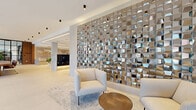 The Forte's lobby in Hackensack, NJ, makes an immediate impression with its expansive, open layout spanning a substantial footprint across a single floor. The entrance features floor-to-ceiling glass doors and large windows that flood the interior with natural light while offering views of the surrounding streetscape, creating a welcoming and airy atmosphere from the moment you step inside.

The design is anchored by large-format white porcelain tile flooring that runs seamlessly throughout, complemented by crisp white ceilings with sleek recessed and surface-mounted lighting. A dramatic textured metallic accent wall serves as a striking focal point in the lounge area, where contemporary seating arrangements with neutral-toned chairs and a warm wood coffee table invite residents to relax.

A refined conference or co-working table — crafted from rich walnut and surrounded by cognac leather and brass-framed chairs — sits beneath elegant globe pendant lights, bathed in natural light from oversized windows. Warm wood slat paneling lines the elevator vestibule, framing stainless steel elevator doors with polished sophistication.

The lobby's reception desk is clad in veined marble stone, bearing The Forte's branded signage, and is flanked by warm wood paneling and a dedicated package room. A well-organized mailbox station with marble surround and under-lighting completes the thoughtfully appointed space, delivering a seamless blend of style and practicality.
