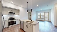 This well-designed two-bedroom, three-bathroom residence in Broomfield, Colorado offers a thoughtfully laid-out single-floor plan with modern finishes throughout. The open-concept kitchen serves as a focal point, featuring a large center island with an undermount sink, sleek quartz countertops, gray shaker-style cabinetry, stainless steel appliances including a refrigerator, range, microwave, and dishwasher, and striking pendant lighting overhead. The kitchen flows seamlessly into the living area, which is bathed in natural light through large windows and a glass door that opens to an outdoor area with views of the surrounding community. Rich hardwood-style flooring extends throughout the main living spaces, adding warmth and continuity. The primary bedroom is a comfortable retreat with a ceiling fan, natural light, and access to a well-appointed en-suite bathroom featuring a soaking tub with marble-style tile surround, a white quartz vanity, large-format tile flooring, and a dedicated walk-in closet. The second bedroom also features hardwood-style flooring, a ceiling fan, and a bright window. Three closets provide generous storage throughout the home, and a hallway connects all spaces efficiently for a functional, cohesive living experience.