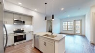 This well-designed two-bedroom, three-bathroom residence in Broomfield, Colorado offers a thoughtfully laid-out single-floor plan with modern finishes throughout. The open-concept kitchen serves as a focal point, featuring a large center island with an undermount sink, sleek quartz countertops, gray shaker-style cabinetry, stainless steel appliances including a refrigerator, range, microwave, and dishwasher, and striking pendant lighting overhead. The kitchen flows seamlessly into the living area, which is bathed in natural light through large windows and a glass door that opens to an outdoor area with views of the surrounding community. Rich hardwood-style flooring extends throughout the main living spaces, adding warmth and continuity. The primary bedroom is a comfortable retreat with a ceiling fan, natural light, and access to a well-appointed en-suite bathroom featuring a soaking tub with marble-style tile surround, a white quartz vanity, large-format tile flooring, and a dedicated walk-in closet. The second bedroom also features hardwood-style flooring, a ceiling fan, and a bright window. Three closets provide generous storage throughout the home, and a hallway connects all spaces efficiently for a functional, cohesive living experience.