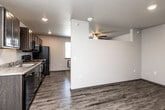 Located at 1360 NE Primrose Ln in Grimes, Iowa, this efficient one-bedroom, one-bathroom unit is thoughtfully designed to maximize every inch of its compact footprint. The open-concept kitchen and living area serves as the heart of the unit, featuring durable wood-style plank flooring, recessed lighting, and a textured ceiling. The kitchen is well-equipped with dark espresso cabinetry, a full suite of black appliances including a refrigerator, range with over-the-range microwave, and dishwasher, along with a sink and ample counter space — all seamlessly flowing into the living area, which is outfitted with a ceiling fan for added comfort. The bedroom offers plush wall-to-wall carpeting, a ceiling fan, and a dedicated closet with sliding doors for convenient storage. Wood-style plank flooring continues into the bedroom's entryway. The bathroom is clean and functional, featuring a full soaking tub and shower combination with bright white surround, wood-style flooring, and the added convenience of a stacked in-unit washer and dryer. A separate utility room rounds out the layout, providing additional practical storage. This unit delivers a modern, move-in-ready living experience in a straightforward, efficient design.