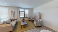 This single-floor residence features a contemporary open-concept layout that seamlessly connects the main living areas. The living room is bright and welcoming, with light hardwood flooring, neutral white walls, and a large window fitted with horizontal blinds that allow natural light to fill the space. Decorative accents, including botanical wall art and a woven area rug, contribute to the room's calm, modern aesthetic. A bar-height kitchen island anchors the transition between the living and kitchen areas, with additional seating provided by stylish counter stools.

The kitchen is well-appointed with dark wood grain cabinetry, a white tile backsplash, light quartz countertops, and a full suite of stainless steel appliances, including a gas range, microwave, and large refrigerator. Recessed lighting illuminates the space effectively. An adjacent dining area benefits from natural light through expansive windows.

Both bedrooms are finished with plush carpet and maintain the unit's neutral color palette. The primary bedroom includes direct access to a spacious walk-in closet with built-in shelving and hanging rods. The bathroom features light wood-look flooring, clean white walls, and modern brushed metal fixtures, completing this well-designed residence.