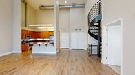 Located at 1201 Race St in San Jose, CA, this two-story residence offers one bedroom and two bathrooms across a well-designed layout. The main floor commands the majority of the living space and immediately impresses with soaring double-height ceilings that flood the open-concept living and dining area with natural light through tall clerestory windows. Light hardwood flooring runs throughout the main level, enhancing the bright and airy atmosphere. French doors provide additional access to the outdoors and contribute to the open feel of the living room. The kitchen is a standout feature, boasting warm honey-toned wood cabinetry, dark granite countertops, stainless steel appliances including a refrigerator and range, and a central island with a built-in sink — ideal for both cooking and casual dining. One full bathroom on the main level features a walk-in glass-enclosed shower with built-in shelving and chrome fixtures. The upper floor houses the bedroom, carpeted for comfort, with a window providing natural light. An en-suite full bathroom offers a vanity with a wide mirror, white cabinetry, and a shower-tub combination. The overall ambiance is clean, modern, and well-lit, with a neutral color palette throughout.