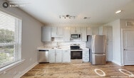 Located at 2828 Pickett Rd in Durham, NC, this single-floor, one-bedroom, one-bathroom unit offers a well-designed layout that maximizes functionality. The open living and kitchen area features warm hardwood-style flooring, a ceiling fan, and a large window that invites generous natural light and outdoor views of the surrounding greenery. The kitchen is equipped with stainless steel appliances, including a range, microwave, and dishwasher, complemented by gray cabinetry, a classic white subway tile backsplash, and track lighting overhead.

A bright, well-lit hallway with a sliding barn door leads to the private quarters. The spacious bedroom is finished with plush carpeting, a ceiling fan, and a set of interior clerestory windows that allow light to pass between spaces while maintaining privacy. The bedroom connects directly to the full bathroom, which features large-format tile flooring, a white vanity with quartz-style countertops, brushed nickel fixtures, and a framed mirror with vanity lighting above.

The unit presents a clean, contemporary aesthetic throughout, with neutral gray walls, white trim, and consistent modern finishes, making it a practical and attractive space in the Durham area.