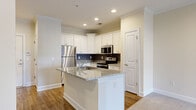 This thoughtfully designed one-bedroom, one-bathroom residence in Sumter, South Carolina offers a comfortable and modern living environment across a single floor. The open-concept layout seamlessly connects the kitchen and living area, creating a cohesive and functional space.

The kitchen is a standout feature, showcasing crisp white shaker-style cabinetry, granite countertops, and a dark subway tile backsplash that adds a contemporary contrast. A peninsula island with a granite surface provides additional prep space and casual seating. Stainless steel appliances, including a refrigerator, range, and built-in microwave, complete the well-equipped kitchen. Warm hardwood-style flooring runs throughout the kitchen area.

The generously sized living room is finished with plush neutral carpet and crowned with elegant crown molding. A ceiling fan with a light fixture adds both style and functionality, while a set of French doors with decorative glass panels floods the room with natural light and offers outdoor access.

The bedroom is a comfortable retreat with soft carpeting, ample closet access, and a clean, neutral palette. The bathroom features white shaker vanity cabinetry, granite countertops, a large mirror, and warm wood-look flooring. A hallway with a dedicated closet provides additional storage. Crown molding details and consistent neutral tones throughout lend the space a polished, cohesive aesthetic.