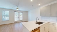 Located at 4939 Ohear Ave in North Charleston, SC, this efficiently designed single-floor unit offers a clean, contemporary aesthetic throughout. The open-concept kitchen and living area forms the heart of the space, featuring light-toned luxury vinyl plank flooring that runs seamlessly from room to room. The kitchen is well-appointed with white shaker-style cabinetry, a white quartz peninsula with an undermount sink, subway tile backsplash, and a full suite of stainless steel appliances including a French door refrigerator with water dispenser, electric range, over-the-range microwave, and dishwasher. The adjoining living area is bright and airy, illuminated by recessed lighting and a ceiling fan, with natural light streaming in through a side window and a set of glass French doors that open to a private exterior balcony. The bathroom maintains the unit's clean, modern palette with a floating white vanity, recessed lighting, and light wood-tone flooring. A dedicated walk-in closet provides practical storage with multi-tiered wire shelving. The entire unit reflects a fresh, move-in-ready finish with crisp white walls, consistent flooring, and thoughtful modern details throughout.
